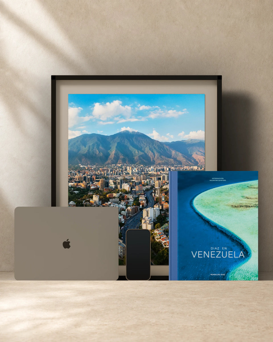 Comparación de escala: el libro Diaz en Venezuela de 26 × 32 cm junto a un fine art print de 40 × 50 cm enmarcado, una MacBook Air de 13 pulgadas y un iPhone 16 Pro